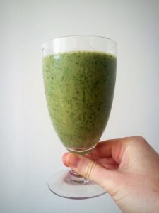 hand holding a green smoothie in clear glass