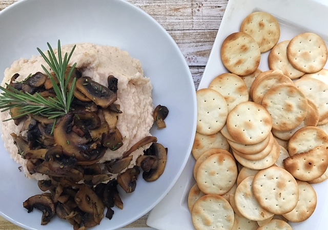 white bean hummus with warm garlic rosemary mushrooms and crackers on white platter and wood background
