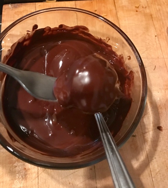 peanut butter banana truffle being dipped in melted dark chocolate 