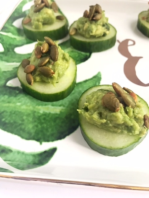 Guacamole and pepita topped cucumber coins on white and green platter