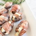 blue cheese and rosemary stuffed dates wrapped in prosciutto on a white platter with rosemary sprig and marble background