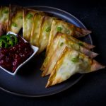 Chicken triangle wontons with cranberry chutney dipping sauce on dark platter and background