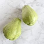 two whole green unpeeled chayote squashes on white marble background