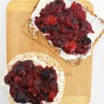 bamboo cutting board withcrispbread and brown rice cake topped with mixed berry chia jam and mascarpone cheese