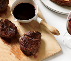 bison steaks on wood cutting board with bowl of fig balsamic sauce