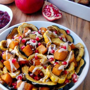 roasted squash and pomegranate seeds in white dish and whole pomegranate fruit on the side
