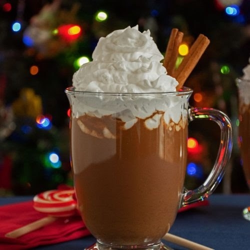 gingerbread hot cocoa in glass mug topped with whipped cream and in front of christmas tree with lights