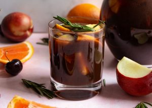 virgin prune sangria in glass mug surrounded by oranges, apples and rosemary sprigs