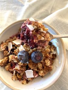 berry crumble in white bowl garnished with fresh blueberries