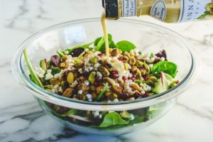 winter salad with pomegranate seeds and pistachios in glass salad bowl and dressing being poured over the top