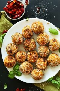 sun-dried tomato vegan meatballs on white platter with fresh basil leaves