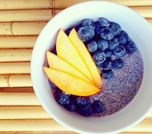 white bowl with maple cardamom chia pudding, fresh blueberries and mango on top of a bamboo background