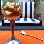 pumpkin pie yogurt parfait in a wine glass on a coffee table outside with blue and white striped patio furniture