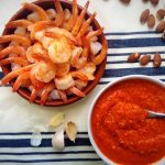 shrimp cocktail in spanish cazuela and romesco sauce in white bowl on white and blue striped towel