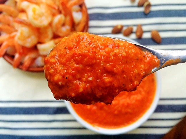 romesco sauce on spoon and shrimp cocktail on a blue and white striped towel