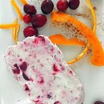 slice of cranberry semifreddo on white plate with orange peel and whole cranberries