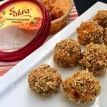 crispy hummus mashed potato balls on a white platter with contain of sabra red pepper hummus in the background