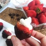 Hand holding Mascarpone Mousse Filled Chocolate Covered Strawberries with strawberries in the background
