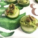 Guacamole and pepita topped cucumber coins on white and green platter