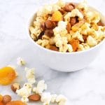 chile lime almond dried apricot popcorn trail mix in white bowl and marble background