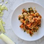 chermoula shrimp on a white plate and white marble background and whole and chopped leeks