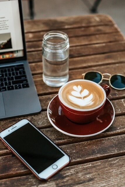 latte, mason jar of water, sunglasses, laptop and cell phone on wooden table