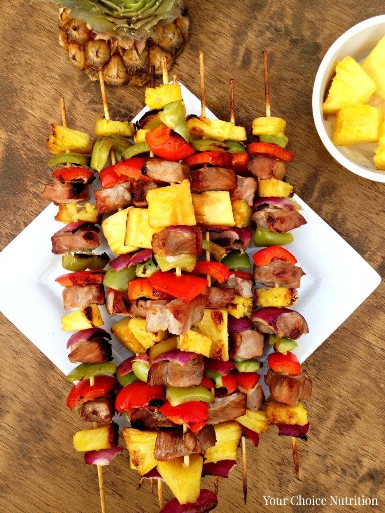 pineapple pork kabobs on a square white plate with peppers