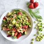 tuna kale edamame strawberry entree salad with dill sprig, chopped cucumber and whole strawberries on white marble background
