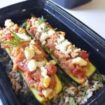 black plastic meal prep container with spiced chicken stuffed zucchini sitting on a bed of dilled brown rice and lentils