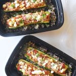 black plastic meal prep container with spiced chicken stuffed zucchini sitting on a bed of dilled brown rice and lentils