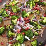 sheet pan with roasted broccoli, sliced red onions, and pomegranate seeds