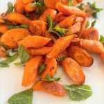 white plate with pieces of roasted carrots and fresh mint leaves